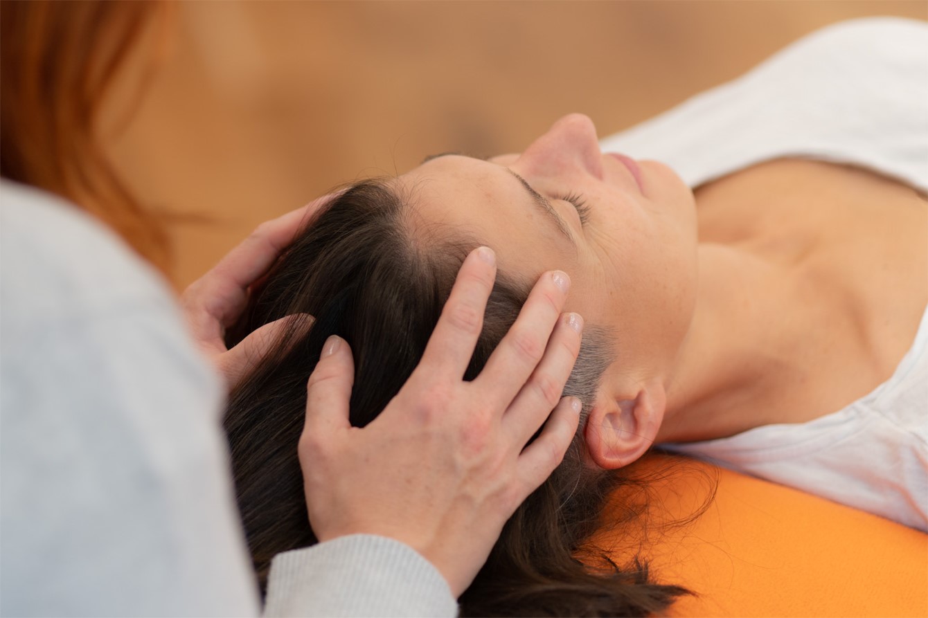 Eine Frau liegt auf einer Behandlungsliege und entspannt bei einer CranioSacralen Berührung